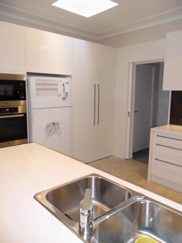 Modern inredning av ett mellanstort kök, med en nedsänkt diskho, vita skåp, bänkskiva i kvarts, glaspanel som stänkskydd, rostfria vitvaror, linoleumgolv och en halv köksö