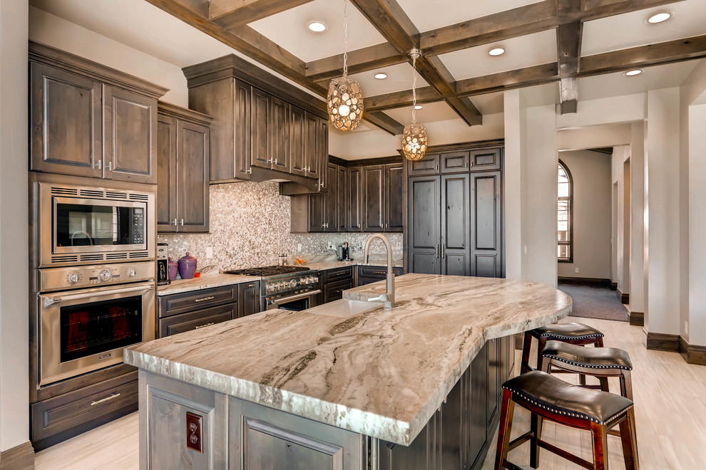 Inspiration for a large transitional u-shaped porcelain tile and beige floor eat-in kitchen remodel in Denver with a farmhouse sink, raised-panel cabinets, dark wood cabinets, limestone countertops, metallic backsplash, mosaic tile backsplash, stainless steel appliances, an island and beige countertops