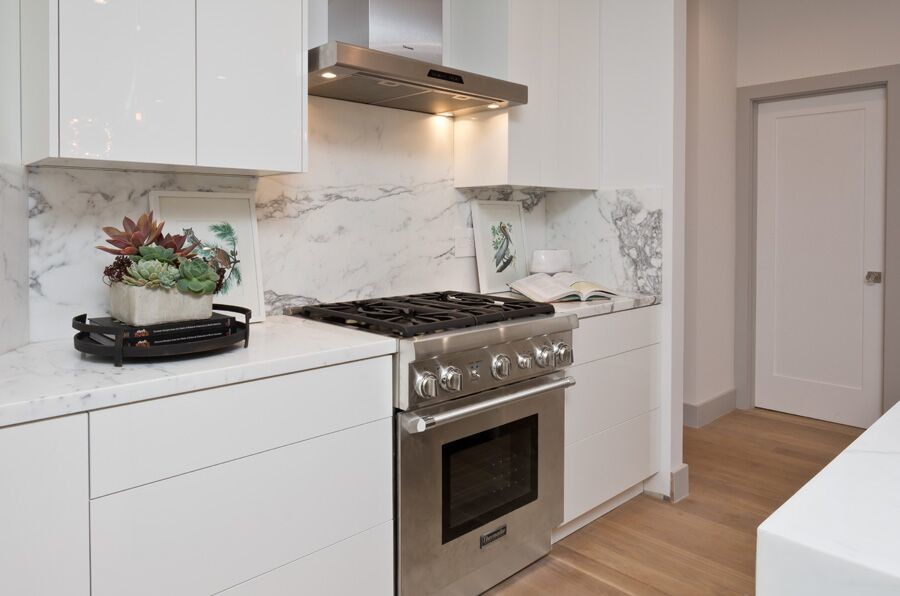 Modern inredning av ett stort kök, med en nedsänkt diskho, släta luckor, vita skåp, marmorbänkskiva, vitt stänkskydd, stänkskydd i marmor, rostfria vitvaror, mellanmörkt trägolv, en köksö och brunt golv