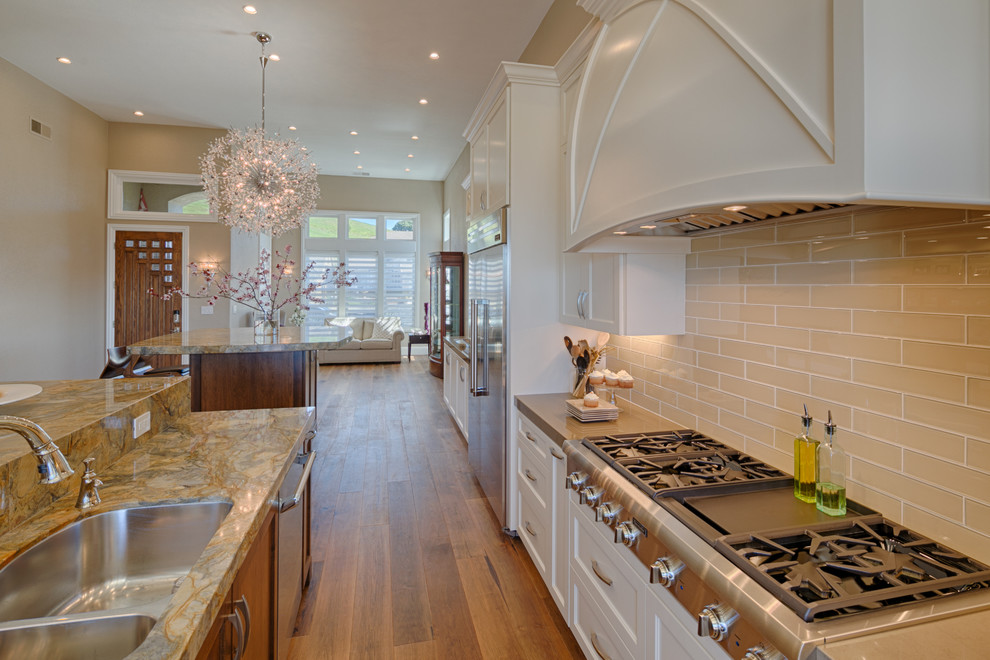 Example of a large beach style galley medium tone wood floor open concept kitchen design in San Francisco with an undermount sink, flat-panel cabinets, white cabinets, beige backsplash, subway tile backsplash, stainless steel appliances and two islands