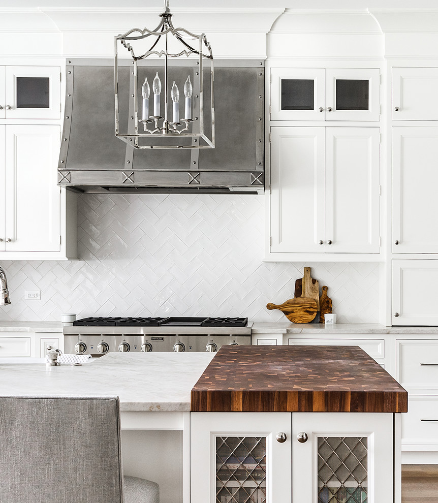 Inspiration for a large traditional kitchen in Chicago with a belfast sink, recessed-panel cabinets, white cabinets, white splashback, metro tiled splashback, stainless steel appliances, dark hardwood flooring and an island.
