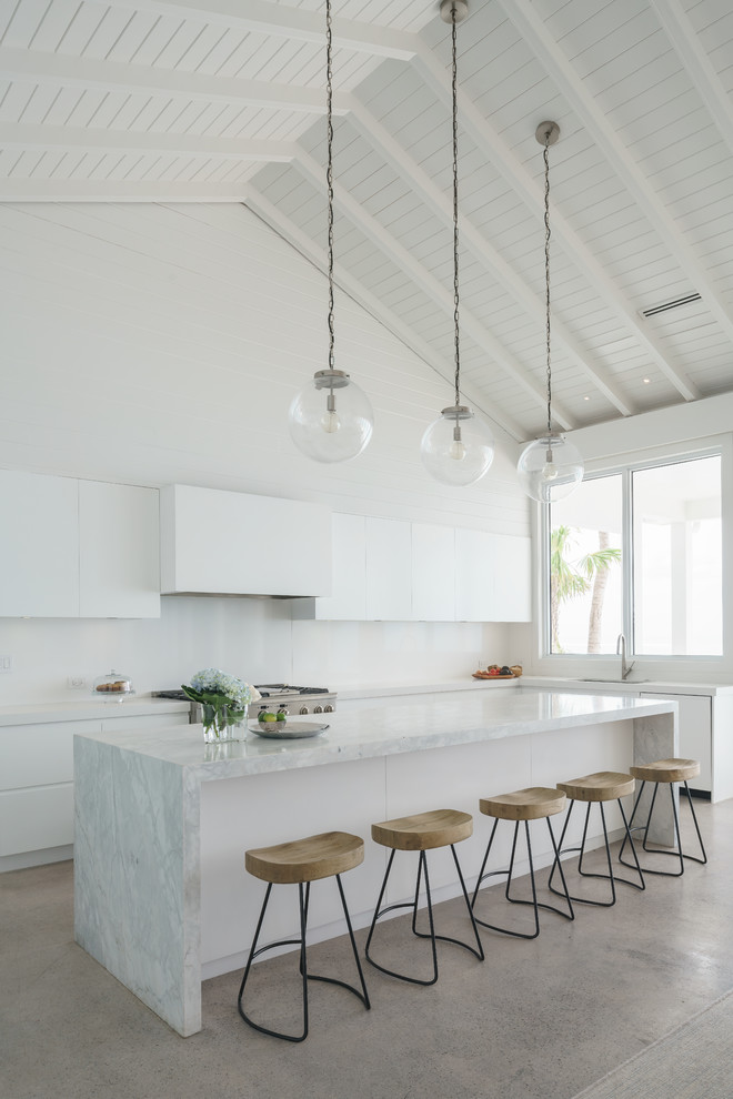 Maritim inredning av ett stort vit vitt kök, med släta luckor, vita skåp, marmorbänkskiva, vitt stänkskydd, betonggolv, en köksö, grått golv och rostfria vitvaror