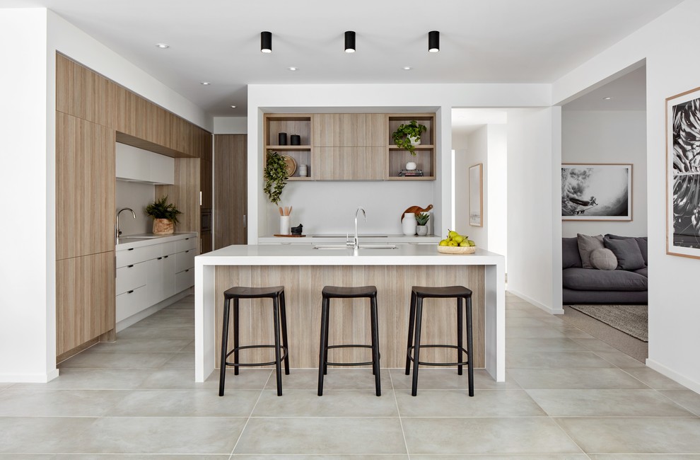 Modern inredning av ett vit vitt l-kök, med en undermonterad diskho, släta luckor, skåp i ljust trä, grått stänkskydd, integrerade vitvaror, en köksö och beiget golv