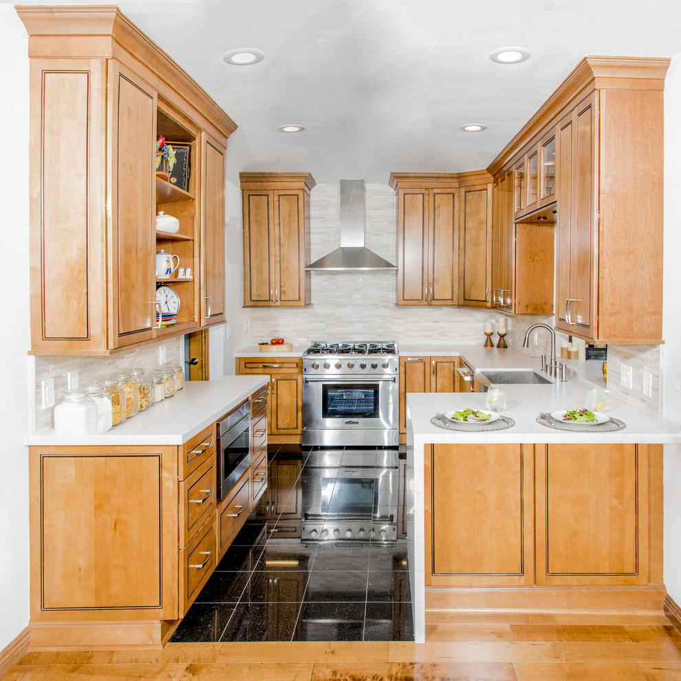Medium sized classic u-shaped kitchen/diner in Los Angeles with a belfast sink, engineered stone countertops, white splashback, porcelain splashback, stainless steel appliances, porcelain flooring, no island, black floors, raised-panel cabinets and light wood cabinets.