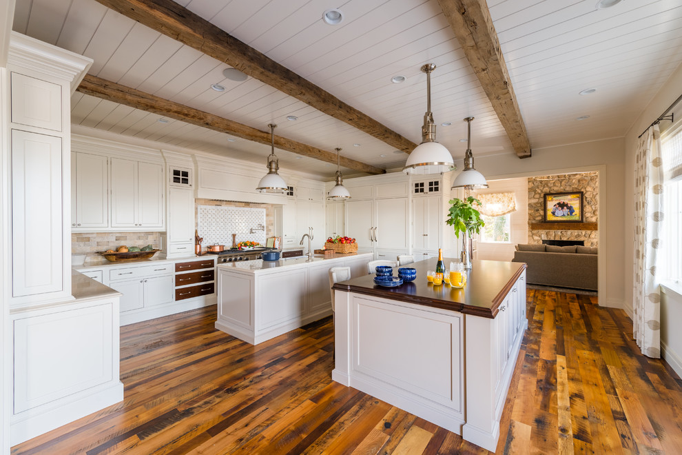 Exemple d'une cuisine chic avec un placard à porte shaker, des portes de placard blanches, une crédence multicolore, un électroménager en acier inoxydable, un sol en bois brun et 2 îlots.
