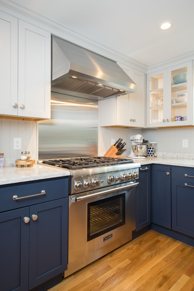 Inspiration for a coastal medium tone wood floor eat-in kitchen remodel in Boston with a farmhouse sink, shaker cabinets, blue cabinets, quartz countertops, gray backsplash, wood backsplash, stainless steel appliances, a peninsula and white countertops