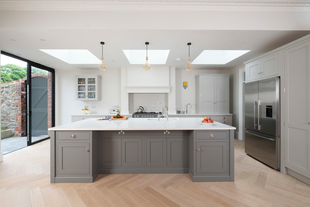 This is an example of a large classic kitchen in Cardiff with shaker cabinets, grey cabinets, quartz worktops, stainless steel appliances, light hardwood flooring, an island, beige floors, white worktops and a submerged sink.