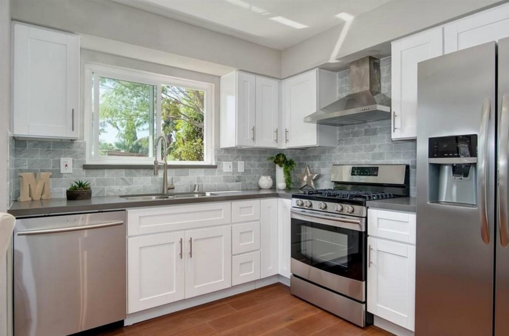 Example of a small trendy l-shaped medium tone wood floor open concept kitchen design in San Diego with an undermount sink, shaker cabinets, white cabinets, quartzite countertops, white backsplash, stone tile backsplash, stainless steel appliances and no island