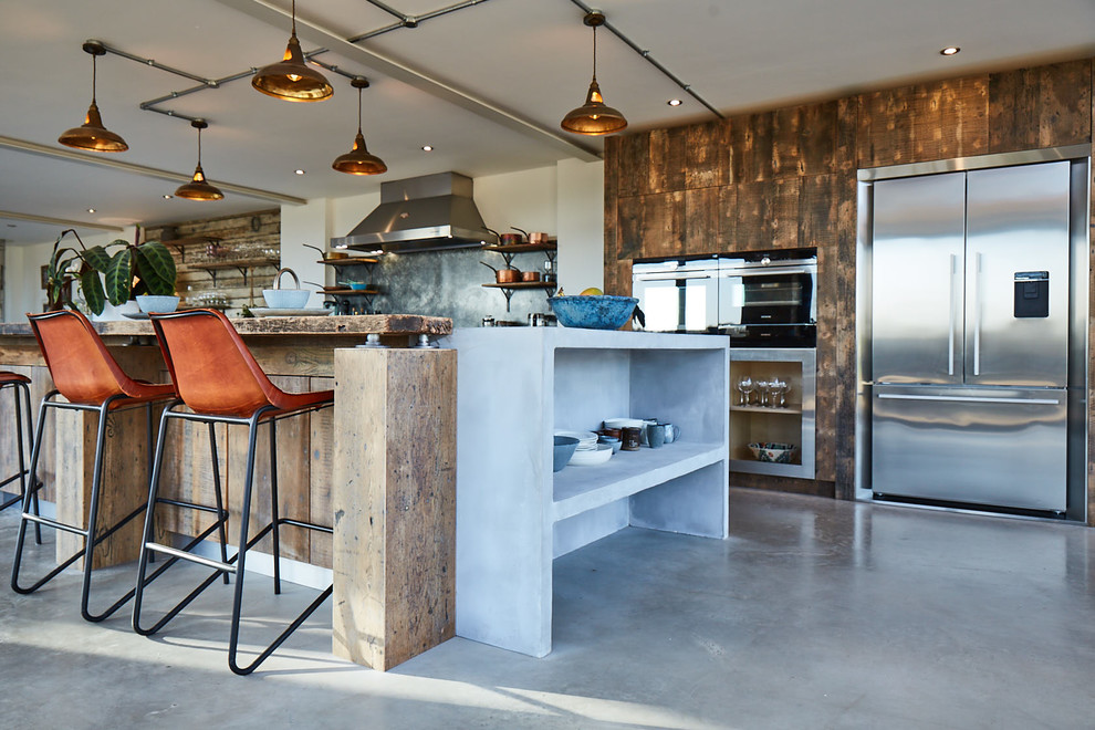 Foto på ett stort industriellt grå kök med öppen planlösning, med en undermonterad diskho, släta luckor, skåp i mellenmörkt trä, bänkskiva i zink, grått stänkskydd, rostfria vitvaror, betonggolv, en halv köksö och grått golv