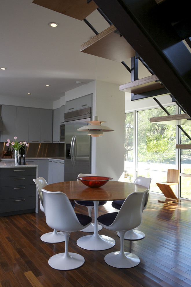 Bild på ett funkis kök och matrum, med rostfria vitvaror, släta luckor, stänkskydd med metallisk yta och stänkskydd i metallkakel
