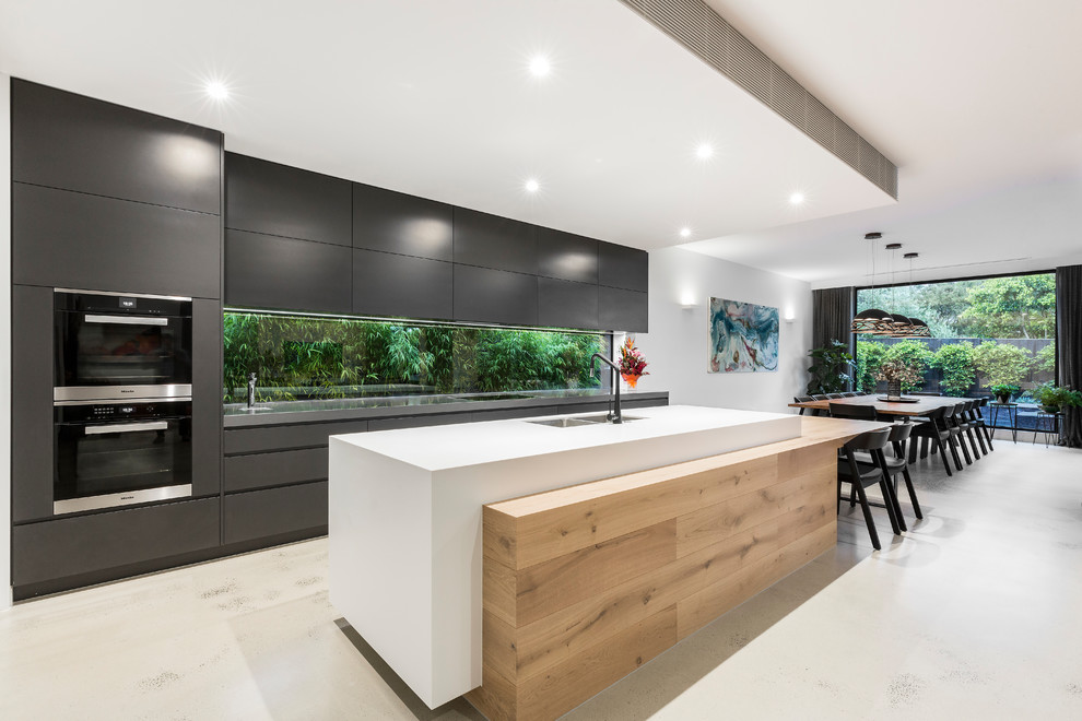 Zweizeilige Moderne Wohnküche mit Doppelwaschbecken, flächenbündigen Schrankfronten, Rückwand-Fenster, schwarzen Elektrogeräten, Kücheninsel, weißem Boden und weißer Arbeitsplatte in Melbourne