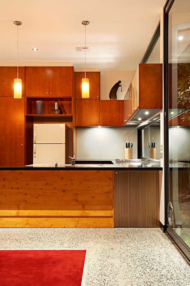 На фото: параллельная кухня среднего размера в современном стиле с фасадами цвета дерева среднего тона, белой техникой, обеденным столом, накладной мойкой, плоскими фасадами, серым фартуком, фартуком из стеклянной плитки и бетонным полом