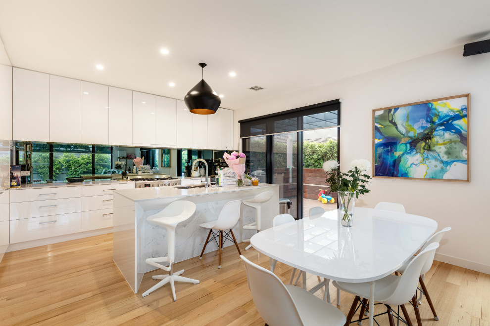 Moderne Küche in L-Form mit Unterbauwaschbecken, flächenbündigen Schrankfronten, weißen Schränken, Küchengeräten aus Edelstahl, braunem Holzboden, Kücheninsel, braunem Boden und weißer Arbeitsplatte in Melbourne