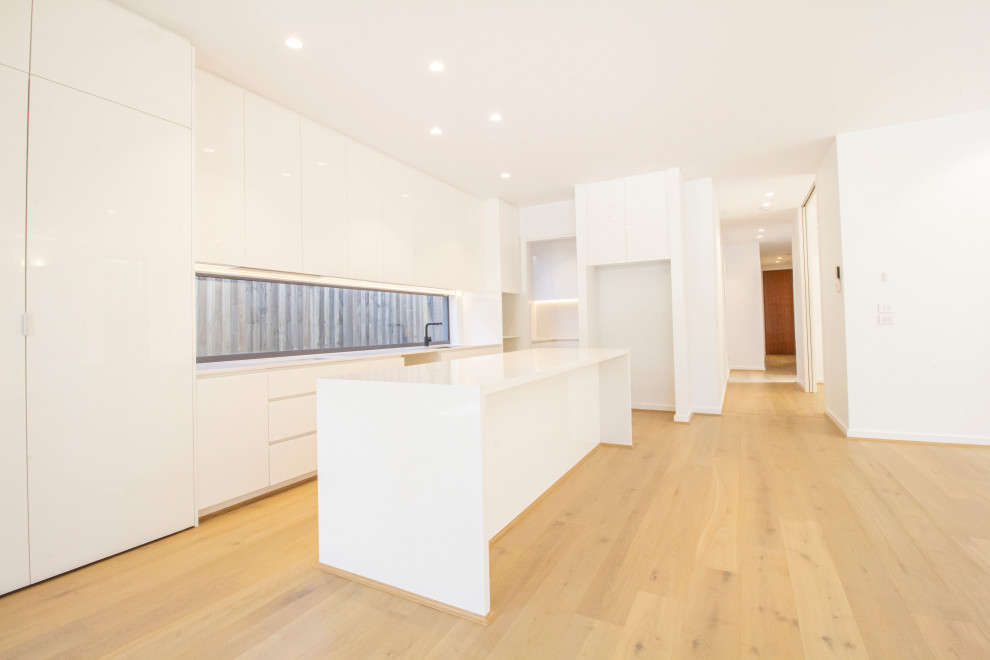 Example of a large trendy galley laminate floor open concept kitchen design in Melbourne with an undermount sink, recessed-panel cabinets, white cabinets, concrete countertops, white backsplash, ceramic backsplash, stainless steel appliances, an island and white countertops