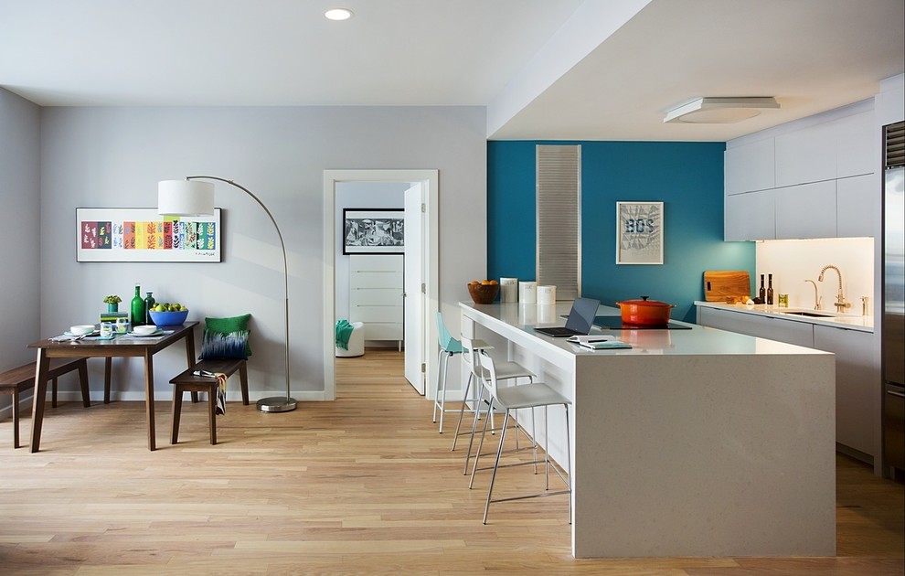 Photo of a medium sized contemporary single-wall kitchen/diner in Boston with a submerged sink, flat-panel cabinets, white cabinets, engineered stone countertops, white splashback, stainless steel appliances, light hardwood flooring and an island.