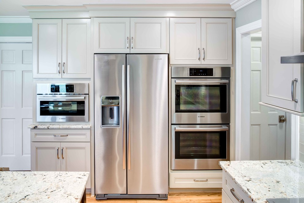 Enclosed kitchen - mid-sized traditional u-shaped medium tone wood floor and brown floor enclosed kitchen idea in Raleigh with an undermount sink, recessed-panel cabinets, white cabinets, granite countertops, white backsplash, glass tile backsplash, stainless steel appliances and an island