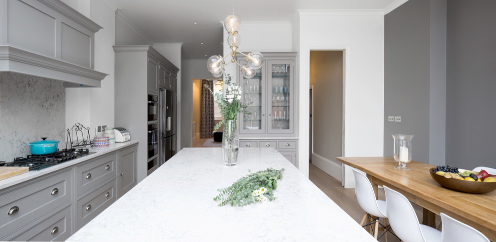 Foto på ett avskilt, stort funkis vit u-kök, med en nedsänkt diskho, luckor med profilerade fronter, grå skåp, marmorbänkskiva, vitt stänkskydd, stänkskydd i marmor, integrerade vitvaror, ljust trägolv, en köksö och brunt golv