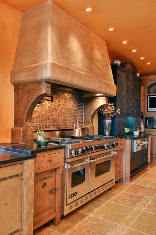 Amerikansk inredning av ett kök, med rostfria vitvaror, skåp i slitet trä, brunt stänkskydd och stänkskydd i mosaik