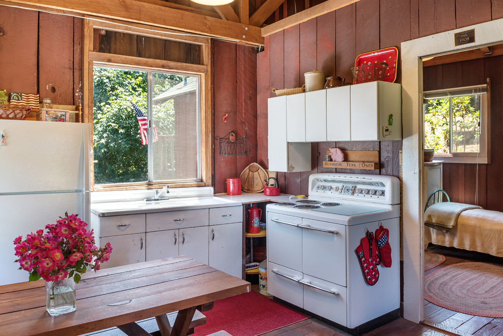 Rustik inredning av ett kök, med släta luckor, vita skåp, vita vitvaror, mörkt trägolv och brunt golv
