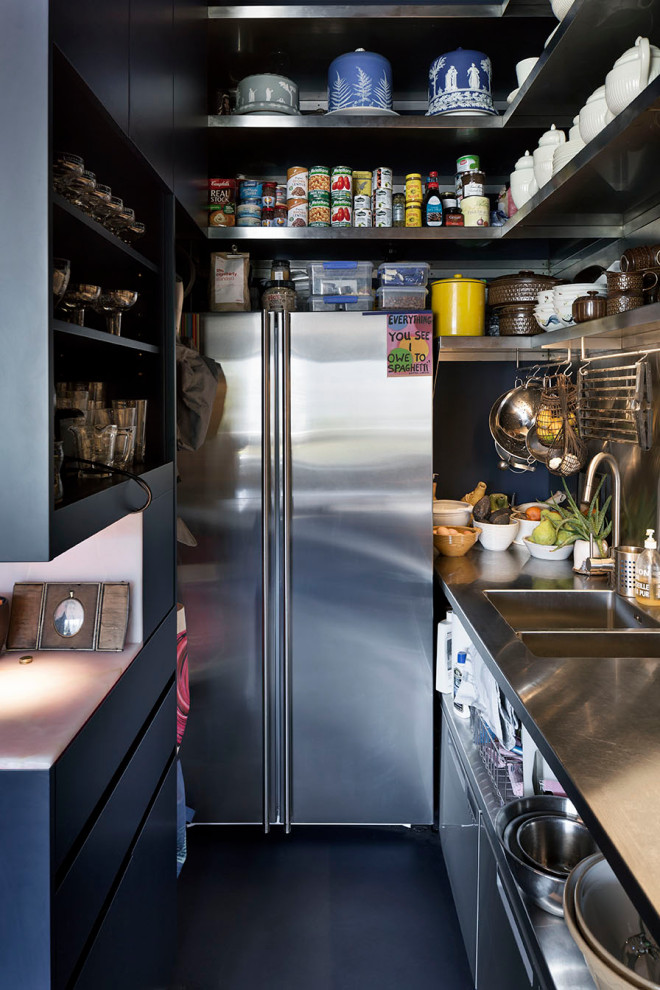 Industriell inredning av ett kök, med en integrerad diskho, bänkskiva i rostfritt stål, stänkskydd med metallisk yta, stänkskydd i metallkakel, rostfria vitvaror, linoleumgolv och svart golv