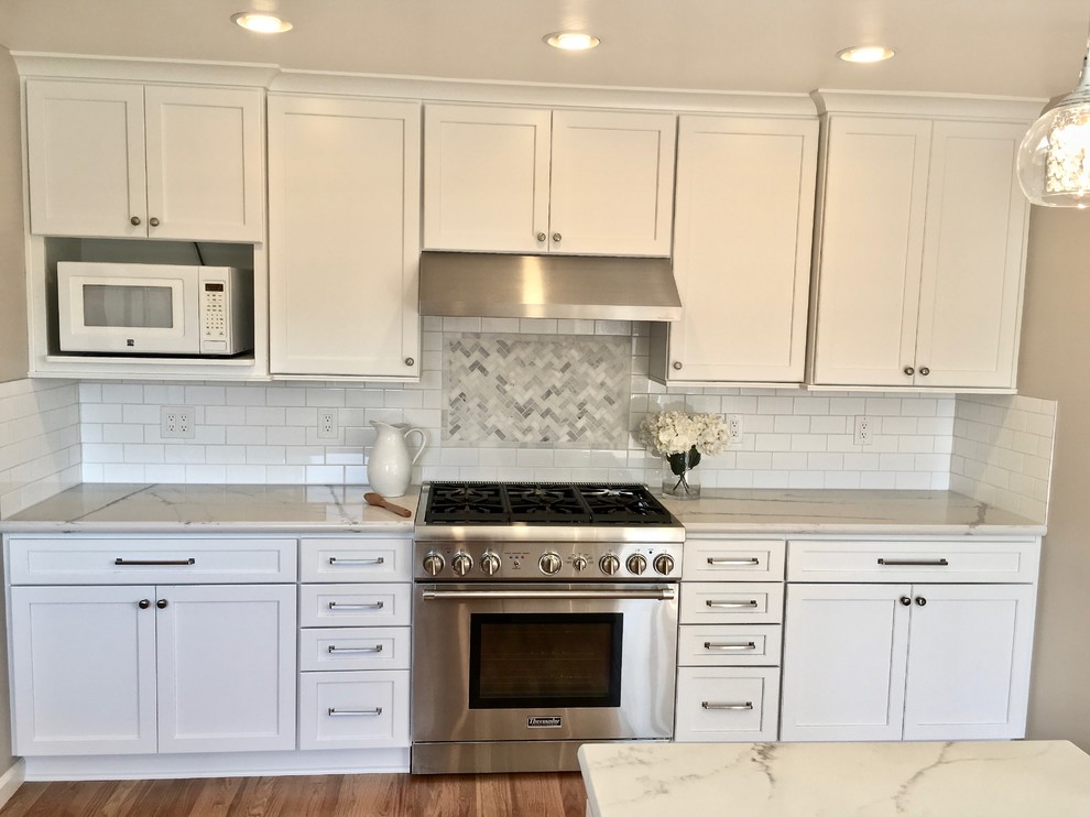 Example of a mid-sized trendy galley medium tone wood floor and brown floor enclosed kitchen design in San Francisco with an undermount sink, white cabinets, solid surface countertops, white backsplash, subway tile backsplash, stainless steel appliances, a peninsula and white countertops