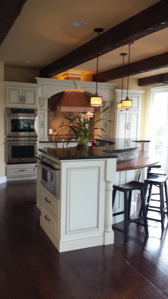 Mid-sized elegant l-shaped medium tone wood floor eat-in kitchen photo in Indianapolis with an undermount sink, raised-panel cabinets, white cabinets, granite countertops, beige backsplash, cement tile backsplash, stainless steel appliances and an island