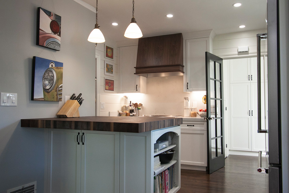 Exempel på ett mellanstort amerikanskt kök, med en undermonterad diskho, luckor med infälld panel, vita skåp, bänkskiva i kvarts, vitt stänkskydd, stänkskydd i sten, rostfria vitvaror, mellanmörkt trägolv, en köksö och brunt golv