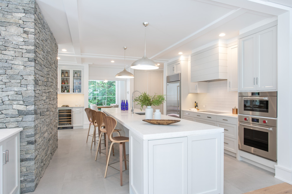 Inspiration for a farmhouse single-wall open plan kitchen in New York with a belfast sink, shaker cabinets, white cabinets, marble worktops, white splashback, ceramic splashback, stainless steel appliances, ceramic flooring, an island, grey floors and white worktops.
