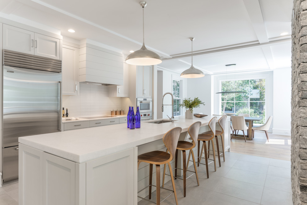 This is an example of a country galley kitchen/diner in New York with shaker cabinets, white cabinets, marble worktops, white splashback, ceramic splashback, stainless steel appliances, ceramic flooring, an island, grey floors, white worktops and a submerged sink.