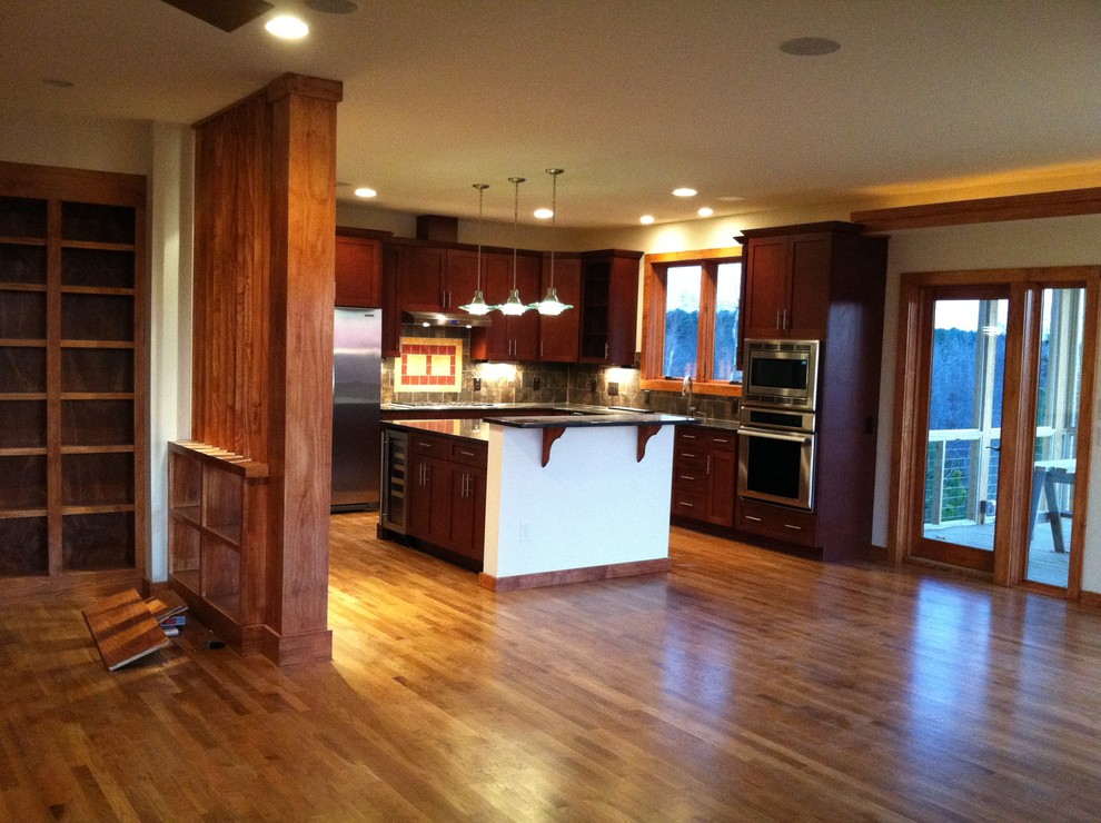 Photo of a large traditional l-shaped kitchen/diner in Raleigh with shaker cabinets, dark wood cabinets, granite worktops, stainless steel appliances, an island and medium hardwood flooring.