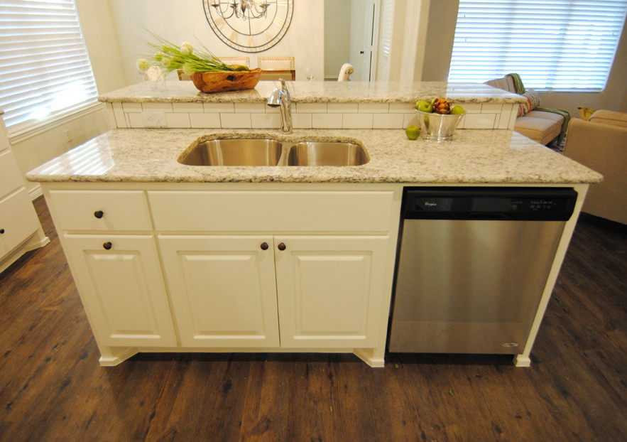 Exempel på ett mellanstort klassiskt kök, med en undermonterad diskho, luckor med infälld panel, vita skåp, granitbänkskiva, vitt stänkskydd, stänkskydd i tunnelbanekakel, rostfria vitvaror, vinylgolv, en köksö och brunt golv