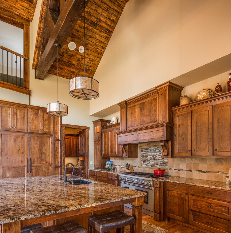 Imagen de cocinas en U rural con fregadero bajoencimera, armarios estilo shaker, puertas de armario de madera oscura, salpicadero beige, electrodomésticos de acero inoxidable, suelo de madera en tonos medios y una isla