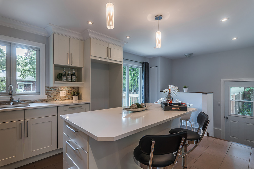 Eat-in kitchen - small contemporary l-shaped porcelain tile eat-in kitchen idea in Montreal with an undermount sink, shaker cabinets, white cabinets, quartz countertops, multicolored backsplash, glass tile backsplash and an island