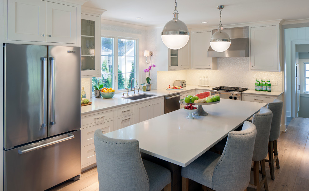 Medium sized traditional kitchen/diner in Grand Rapids with a submerged sink, recessed-panel cabinets, white cabinets, engineered stone countertops, white splashback, mosaic tiled splashback, stainless steel appliances, light hardwood flooring and an island.