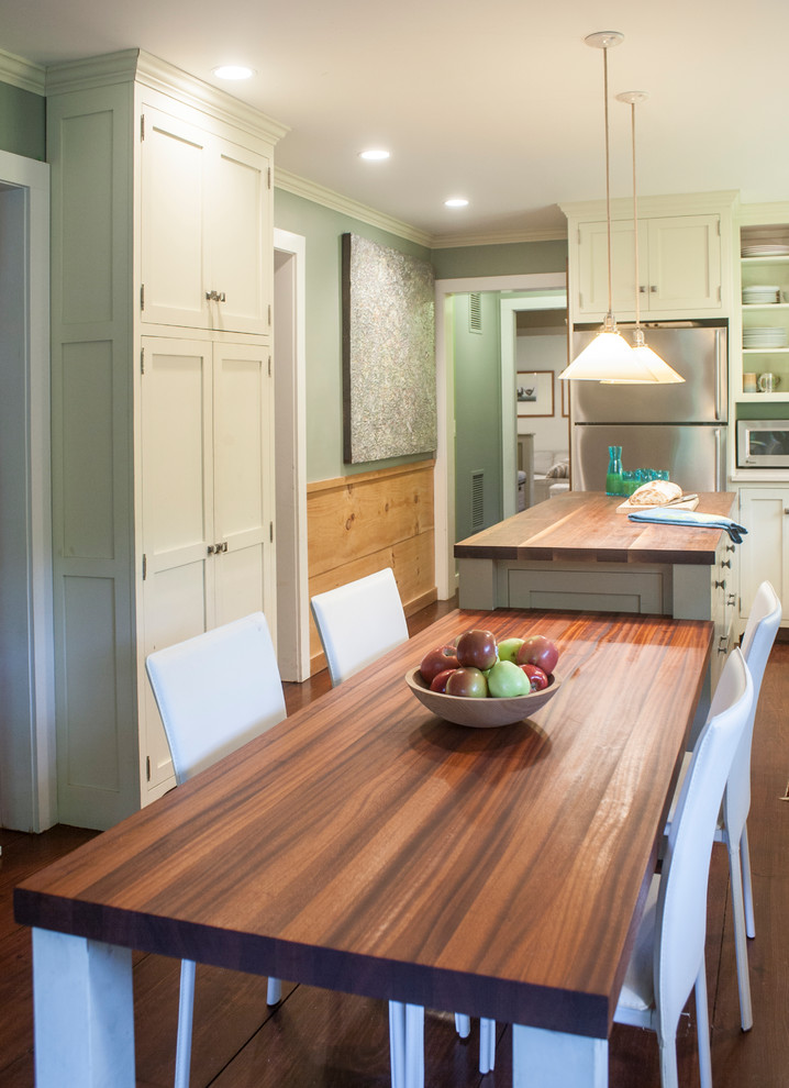 Cette photo montre une cuisine américaine chic avec un placard à porte shaker, des portes de placard beiges, un plan de travail en bois, un électroménager en acier inoxydable et parquet foncé.