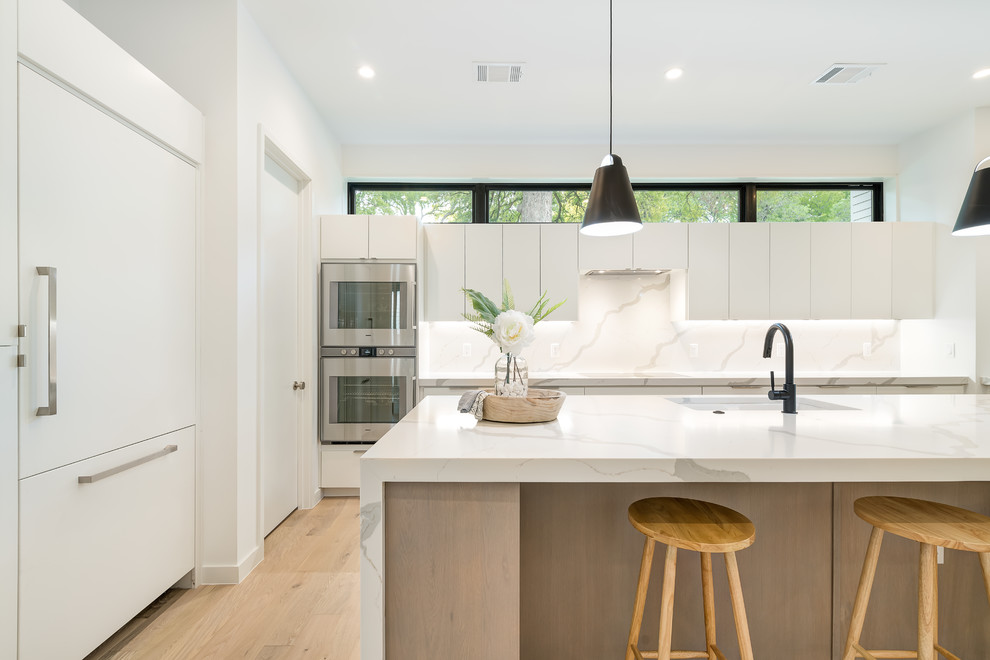 Inspiration for a large scandinavian l-shaped light wood floor and brown floor open concept kitchen remodel in Austin with an undermount sink, flat-panel cabinets, white cabinets, marble countertops, white backsplash, marble backsplash, paneled appliances, an island and white countertops