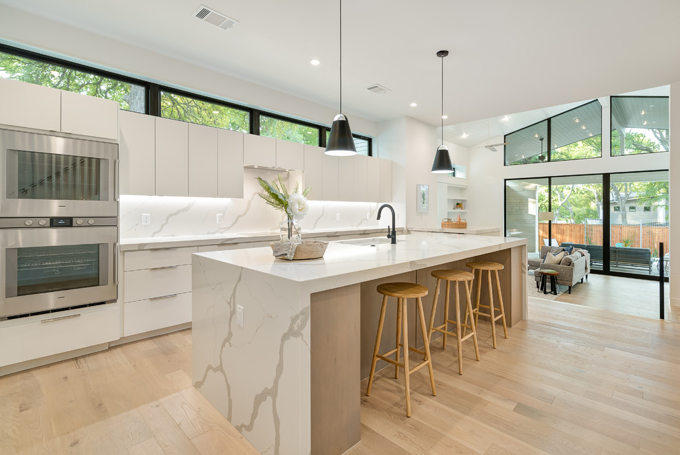 Example of a large danish light wood floor and beige floor open concept kitchen design in Austin with flat-panel cabinets, white cabinets, marble countertops, white backsplash, marble backsplash, stainless steel appliances, an island, white countertops and an undermount sink
