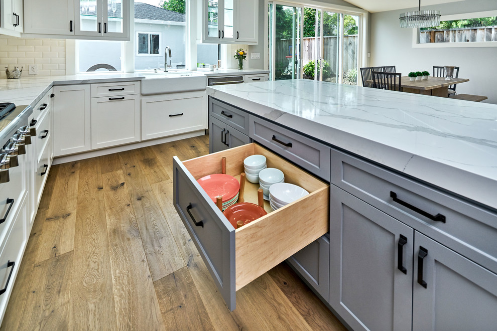 Inspiration for a farmhouse l-shaped medium tone wood floor and brown floor open concept kitchen remodel in San Francisco with a farmhouse sink, shaker cabinets, white cabinets, granite countertops, white backsplash, subway tile backsplash, stainless steel appliances and an island