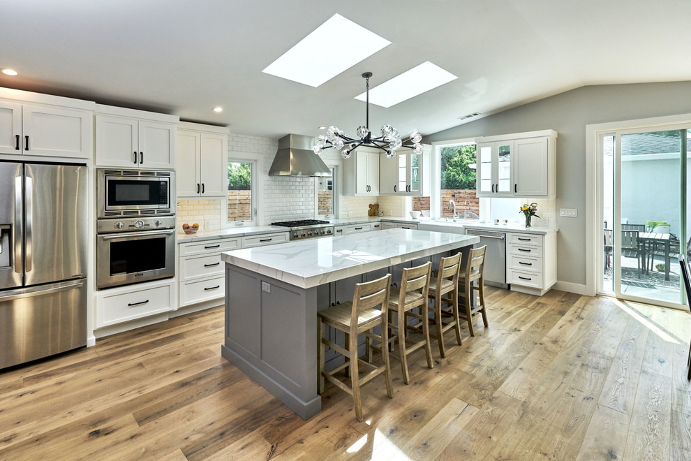Open concept kitchen - farmhouse l-shaped medium tone wood floor and brown floor open concept kitchen idea in San Francisco with a farmhouse sink, shaker cabinets, white cabinets, granite countertops, white backsplash, subway tile backsplash, stainless steel appliances and an island