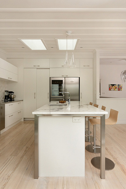 Modern inredning av ett mellanstort kök, med en undermonterad diskho, släta luckor, vita skåp, marmorbänkskiva, vitt stänkskydd, stänkskydd i keramik, rostfria vitvaror, ljust trägolv och en köksö