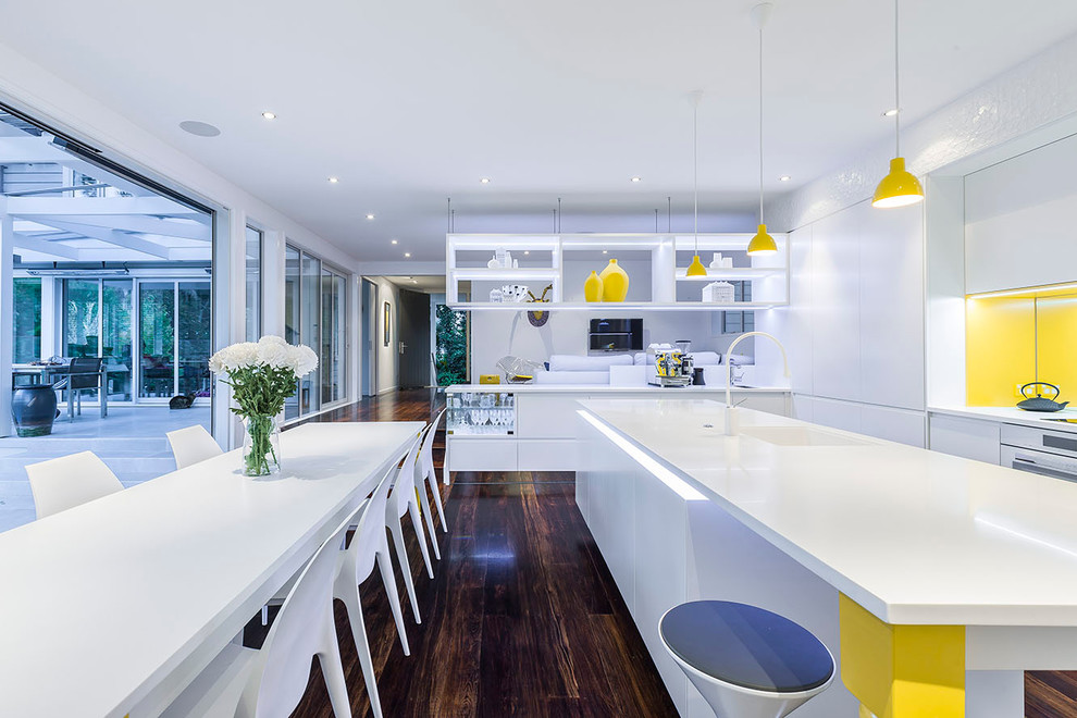 Photo of a contemporary kitchen in Christchurch with a submerged sink, flat-panel cabinets, white cabinets, yellow splashback, white appliances, dark hardwood flooring and multiple islands.
