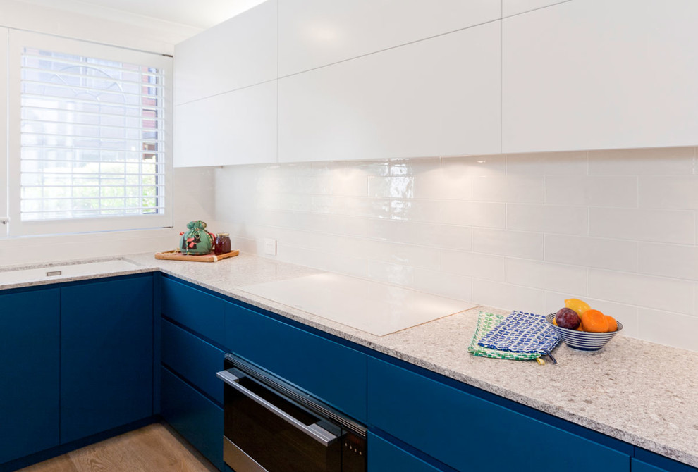 Mittelgroße Moderne Küche in L-Form mit flächenbündigen Schrankfronten, blauen Schränken, Kalkstein-Arbeitsplatte, Küchenrückwand in Weiß, Rückwand aus Metrofliesen, Küchengeräten aus Edelstahl und hellem Holzboden in Sydney