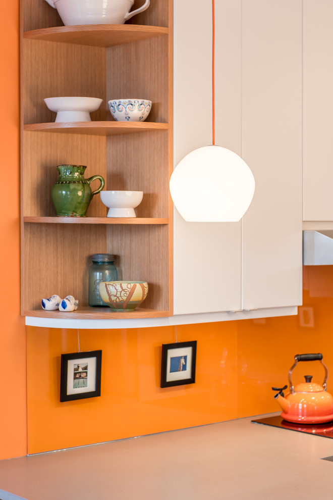 Foto på ett funkis u-kök, med en undermonterad diskho, släta luckor, vita skåp, orange stänkskydd, rostfria vitvaror, ljust trägolv och en halv köksö
