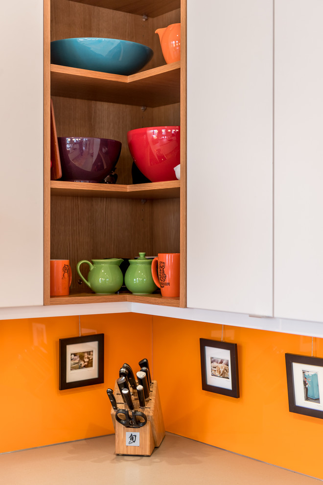 Moderne Küche in U-Form mit Unterbauwaschbecken, flächenbündigen Schrankfronten, weißen Schränken, Küchenrückwand in Orange, Küchengeräten aus Edelstahl, hellem Holzboden und Halbinsel in Philadelphia