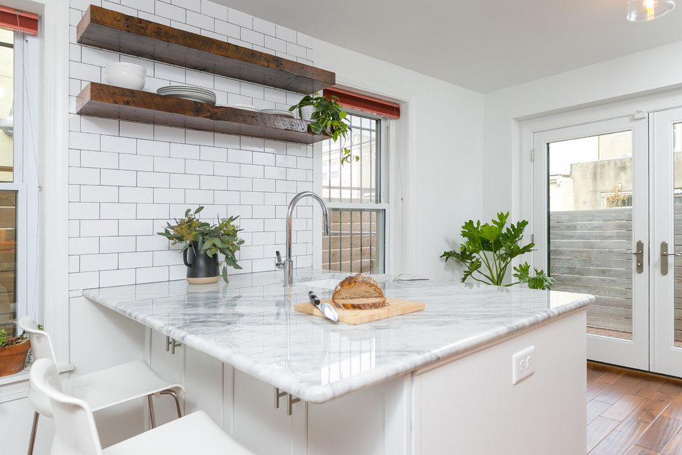 Mid-sized trendy l-shaped medium tone wood floor and brown floor enclosed kitchen photo in Philadelphia with an undermount sink, shaker cabinets, white cabinets, quartzite countertops, white backsplash, subway tile backsplash, stainless steel appliances and a peninsula