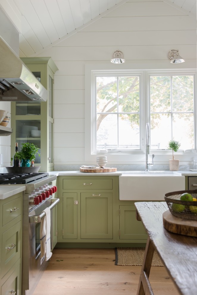 Inredning av ett lantligt kök, med en rustik diskho, skåp i shakerstil, gröna skåp, rostfria vitvaror, mellanmörkt trägolv och en köksö