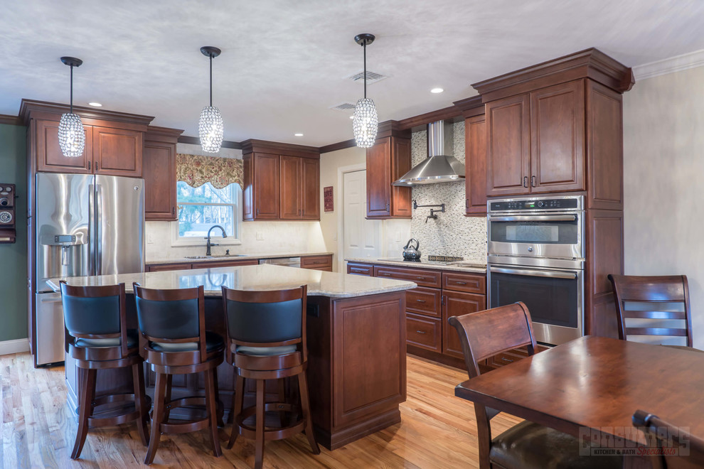 Bild på ett mellanstort kök, med en undermonterad diskho, luckor med upphöjd panel, bruna skåp, bänkskiva i kvarts, grått stänkskydd, rostfria vitvaror, plywoodgolv och en köksö