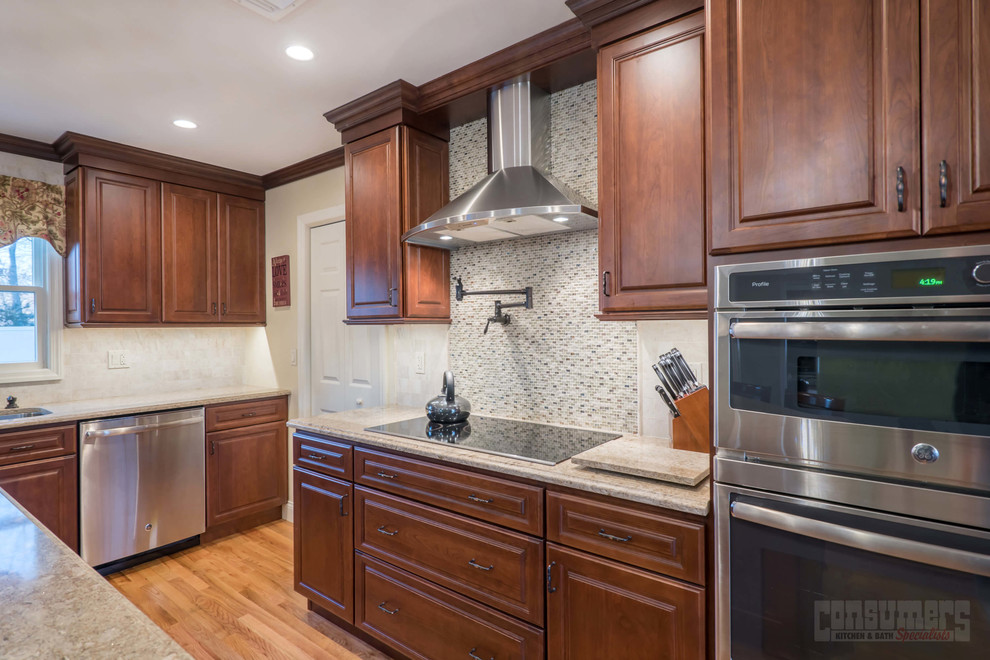Mid-sized l-shaped plywood floor eat-in kitchen photo in New York with an undermount sink, raised-panel cabinets, brown cabinets, quartz countertops, gray backsplash, stainless steel appliances and an island