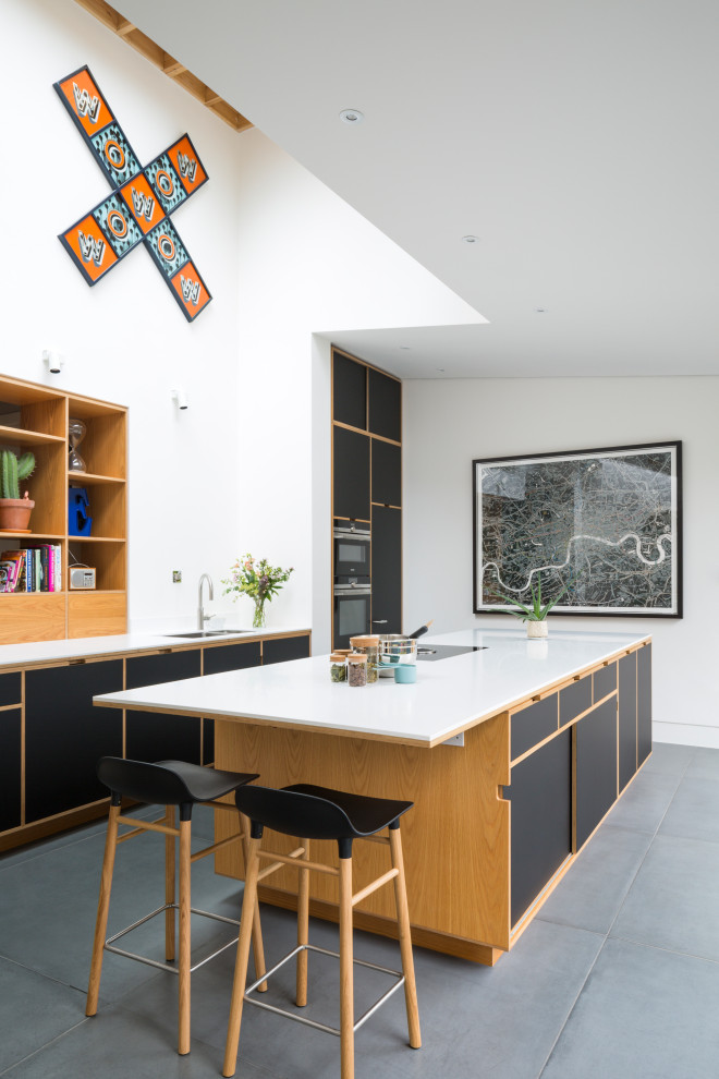 This is an example of a large contemporary galley kitchen in London with a double-bowl sink, flat-panel cabinets, black cabinets, integrated appliances, an island, grey floors and white worktops.
