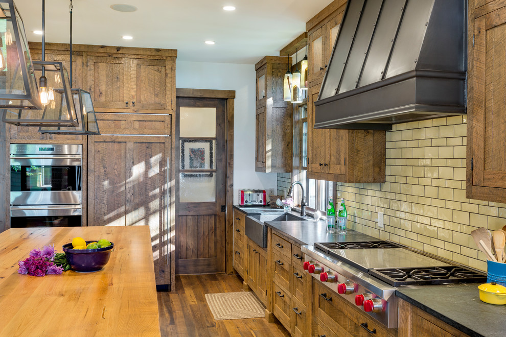 Exempel på ett mellanstort rustikt kök, med en rustik diskho, skåp i shakerstil, skåp i slitet trä, bänkskiva i täljsten, gult stänkskydd, stänkskydd i tunnelbanekakel, integrerade vitvaror, mellanmörkt trägolv och en köksö